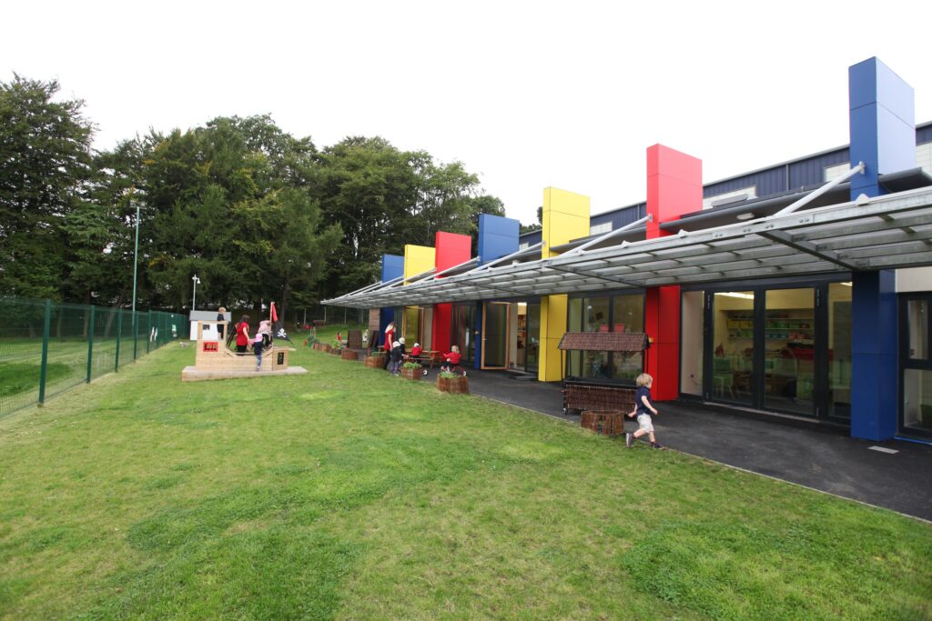 Nursery exterior. Nursery pupils playing outside nursery in play area with staff supervising.