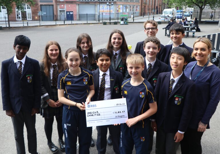 Charities. Pupils on playground with staff member presenting a check for charity.