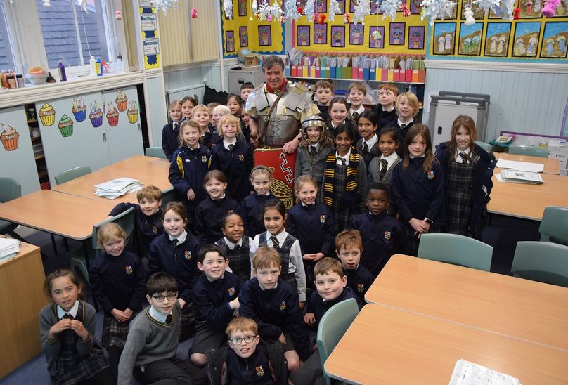 Far From Rome Ancient Soldier Visits HSD Pupils. Historian dressed as roman soldier and pupils in class room standing next to each other.