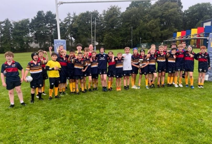 Young Players Serve Up House Rugby Spectacle. Rugby team pupils with trophy standing in line with school sport uniform on looking cheerful, on rugby pitch by rugby goals.